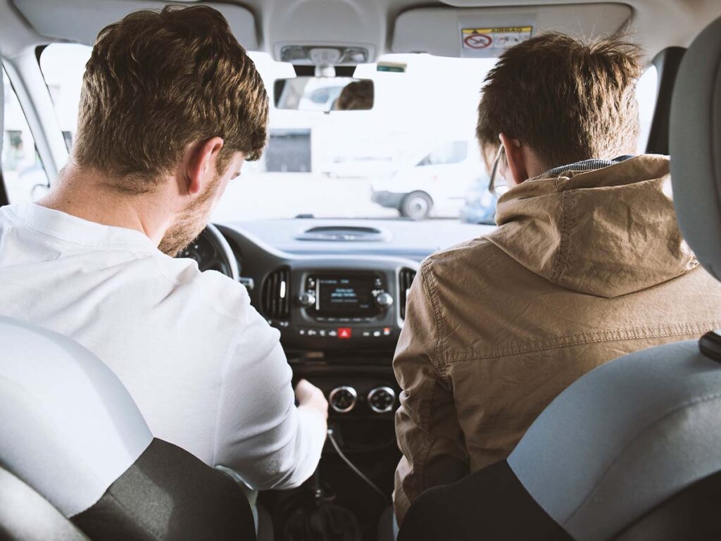 Two men in a car looking at the dashboard.