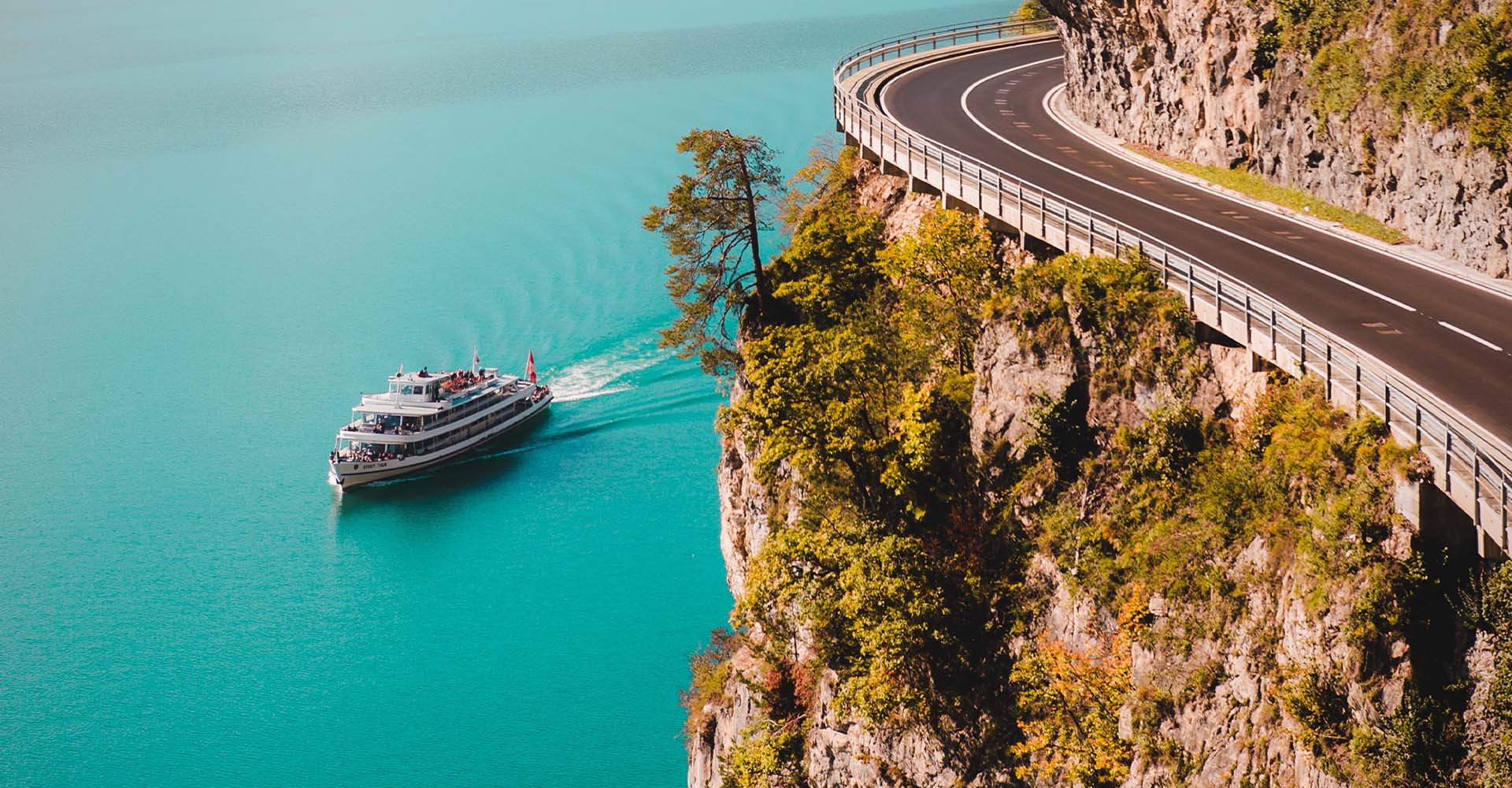 A photo of a winding road near a cliff with a cruise ship in the distance