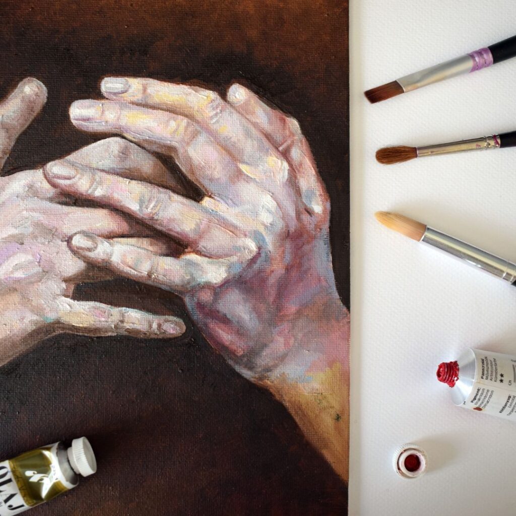 Painting supplies next to a painting of hands
