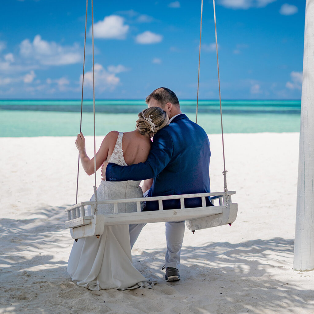 A newlywed couple sitting on a swing at a beautiful beach